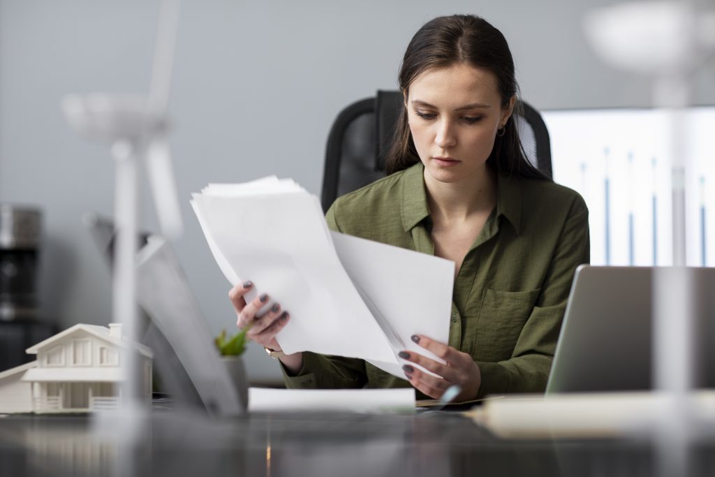 Focused woman going through immigration paperwork at a desk with a laptop and graphs in the background.