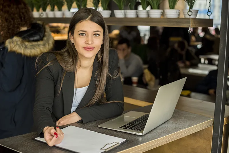 Young woman consultant sitting at a desk with a laptop and clipboard, ready to assist with Canadian immigration services.