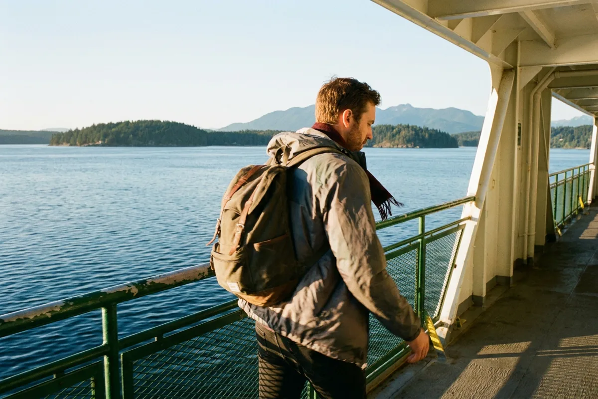 Young worker with a backpack on a B.C. ferry deck looking out over the water and islands